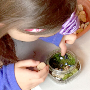 Girl putting moss and plants in a small glass jar