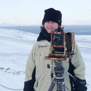 a photo of a smiling woman standing in front of a snow-covered landscape with a camera