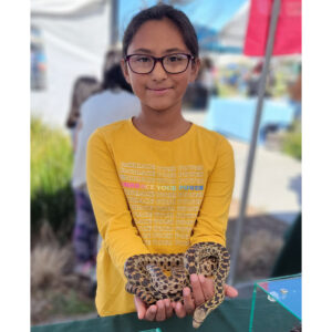 Girl wearing a yellow shirt and glasses smiling and holding a snake