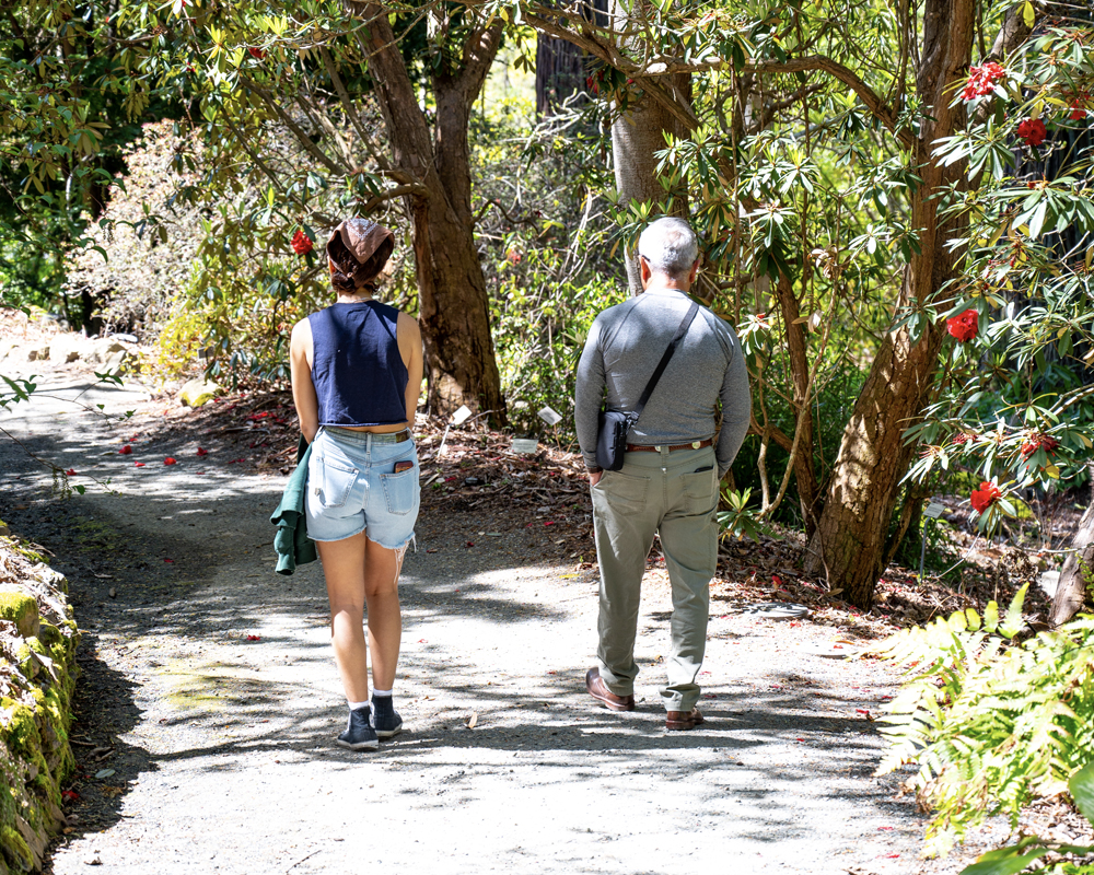 A man and woman are walking together down a sunlit path in the Garden