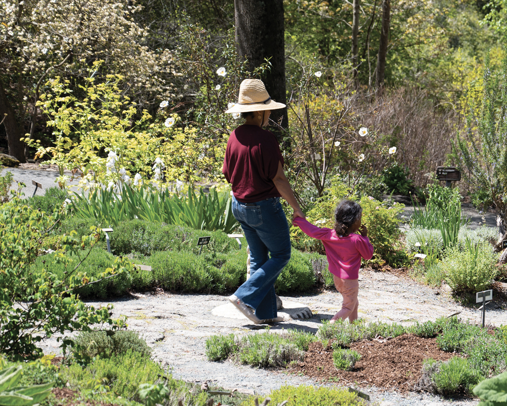 A woman in a large straw hat and her daughter stroll through an herb garden