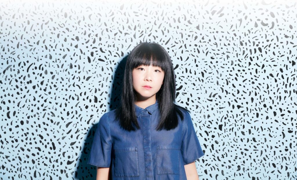 An asian woman wearing a blue blouse standing in front of a white and blue background