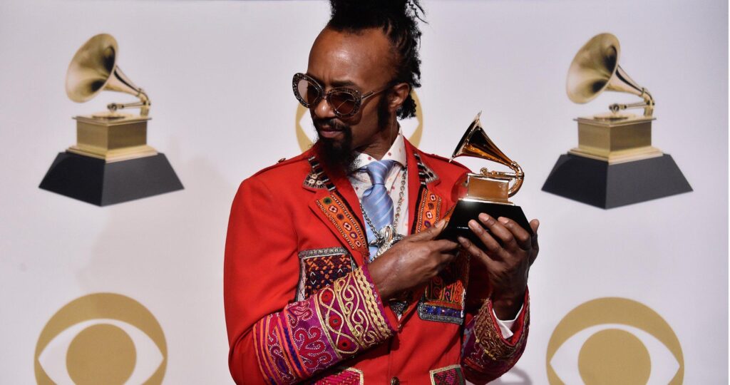 A black man wearing a red jacket holds a music award