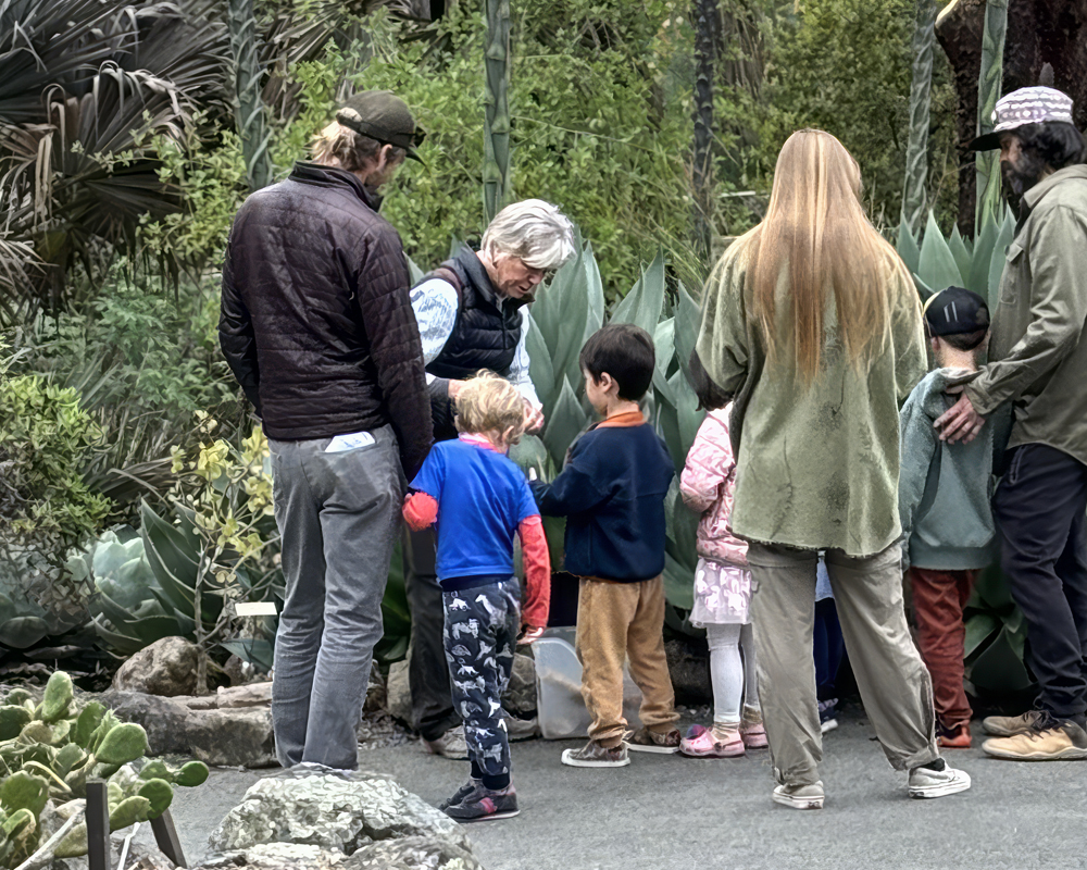 A woman is showing a large plant to a group of children and parents