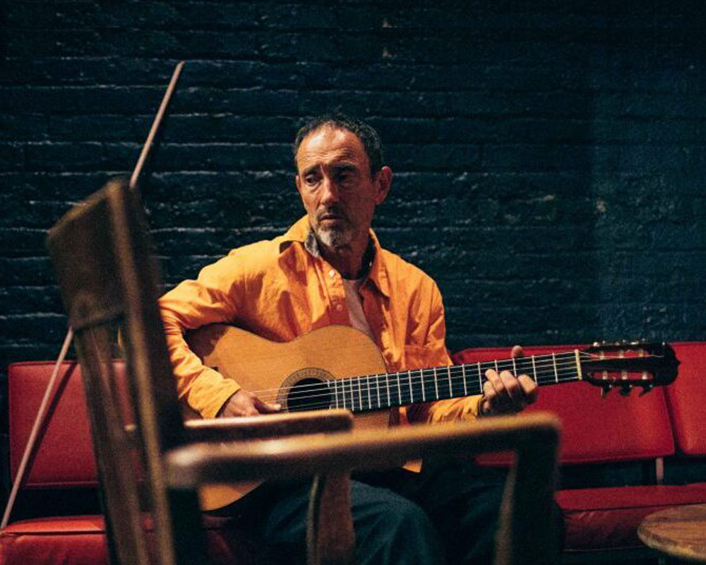 One man wearing an orange shirt plays a guitar