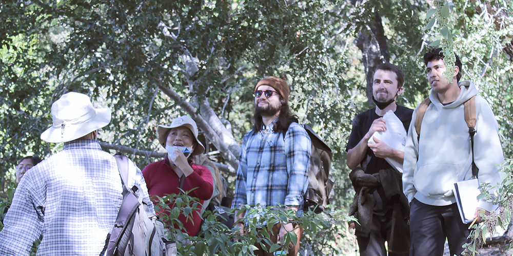 A group of college-age students walk through the Garden carrying notebooks