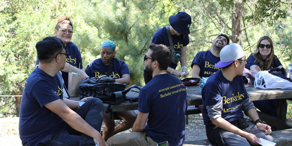 A group of college students in matching blue t-shirts eat lunch at a picnic table