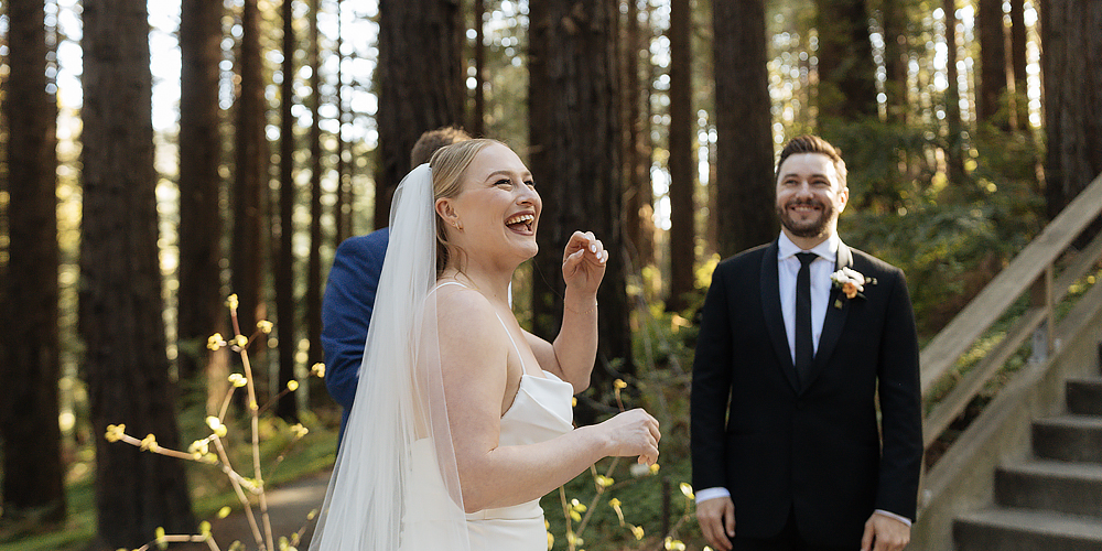 A laughing bride and groom beneath the redwood trees