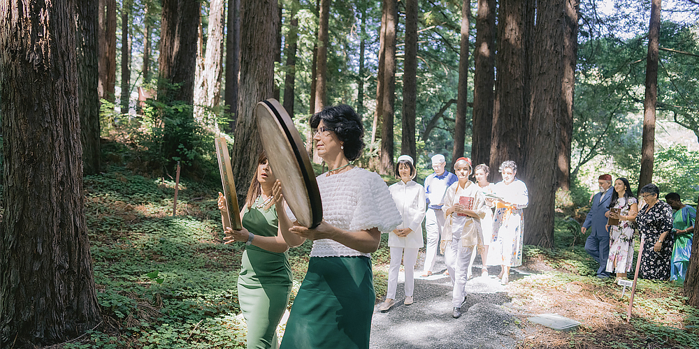 A celebratory procession of people on a path through the redwood grove