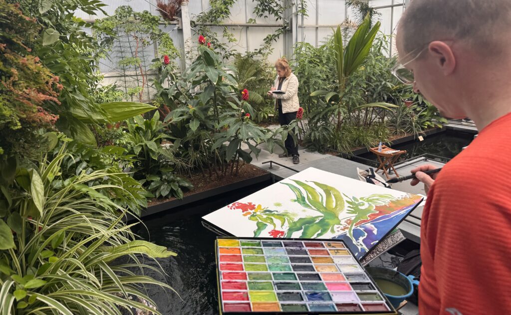 Forest Stearns in the Tropical House with a colorful paint palette and work-in-progress painting.
